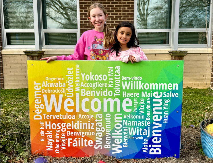 Two students standing behind the welcome sign in front of HMES.